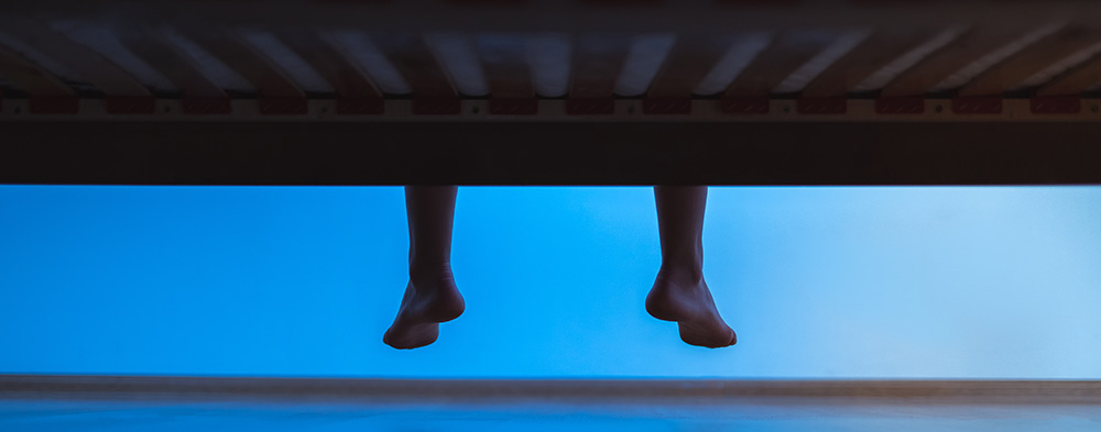Nighttime image of feet hanging off the side of a bed